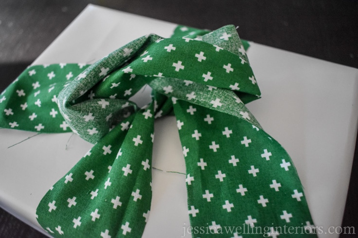 green fabric "ribbon" being tied around white wrapped holiday gift