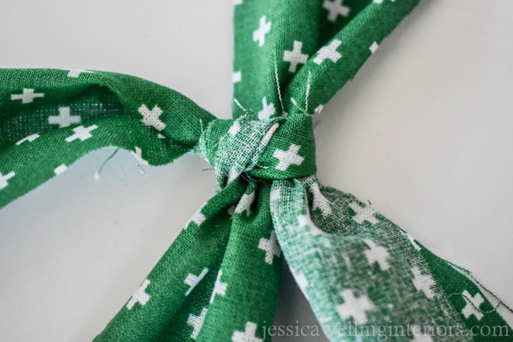 green fabric "ribbon" being tied in a double knot around white paper wrapped Christmas gift