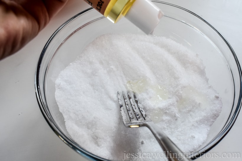 hand adding Vitamin E oil to a bowl of DIY bath salts