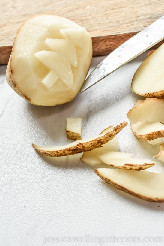 potato being carved into a potato stamp Christmas tree with a pairing knife. Sitting on a wood cutting board