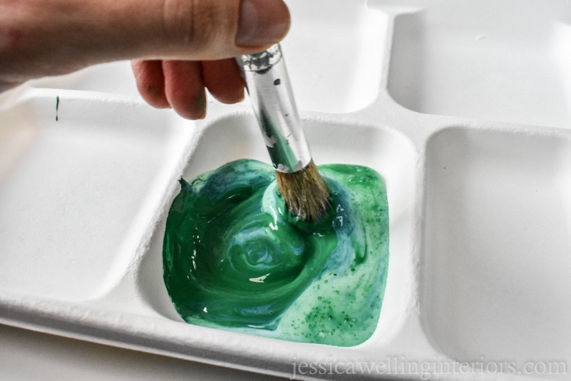 dark green arcrylic paint and fabric medium in a section of a paper tray, being swirled together with a paintbrush