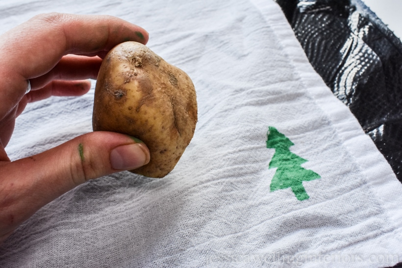 hand holding a potato stamp, ready to print it on a white tea towel