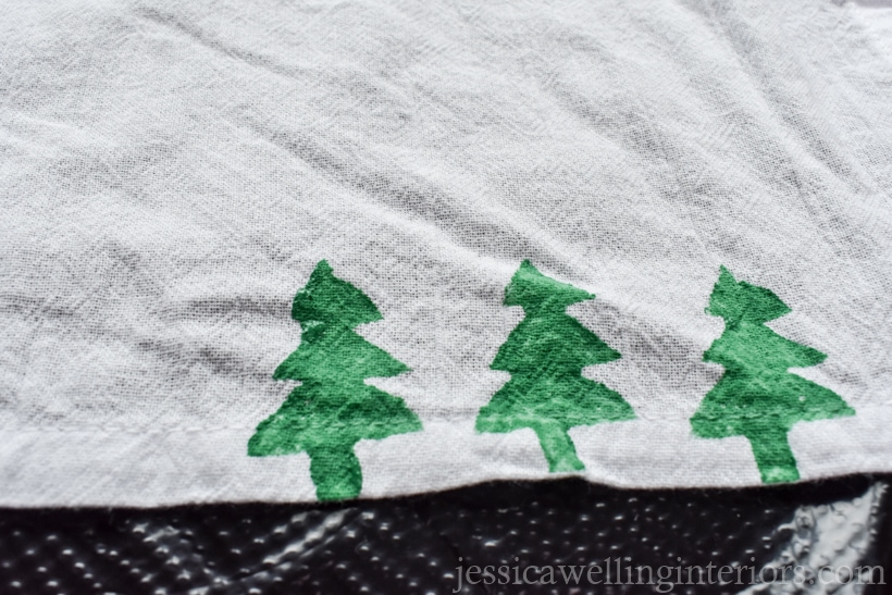 edge of a white tea towel with three green Christmas trees stamped on the bottom