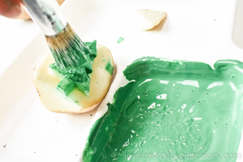 Christmas tree potato stamp being dabbed with green paint using a stencil brush