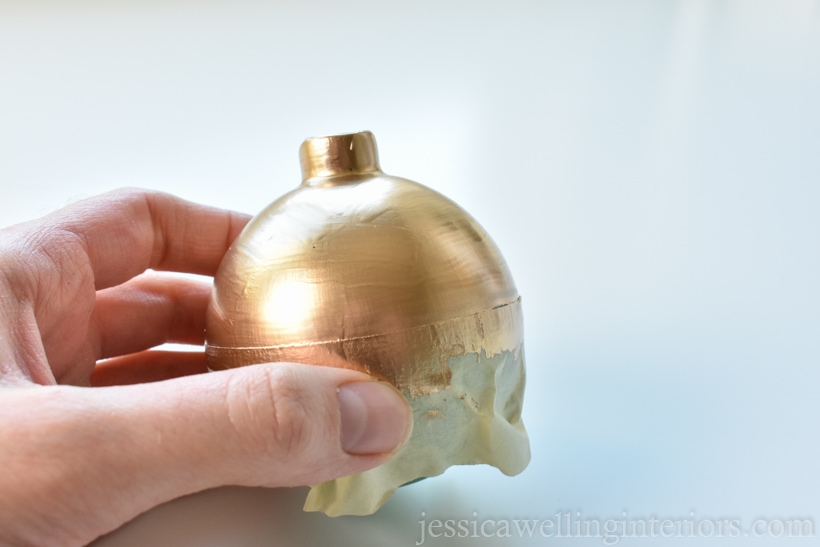 hand holding glass ornament with the top painted gold