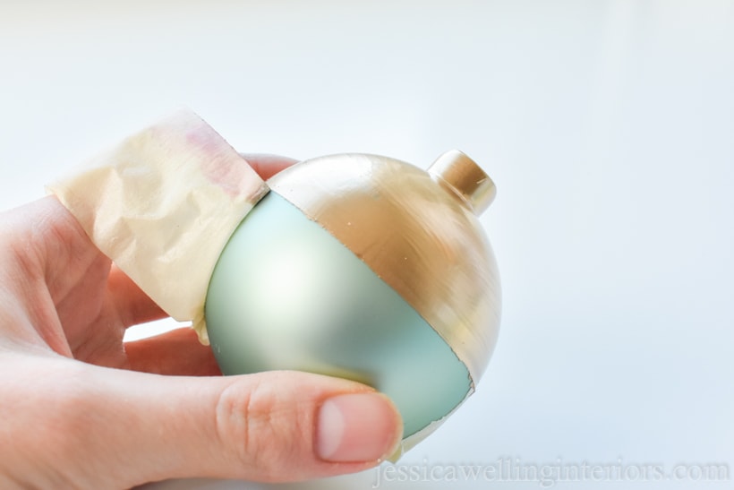 hand holding glass ball ornament and removing masking tape from around the center