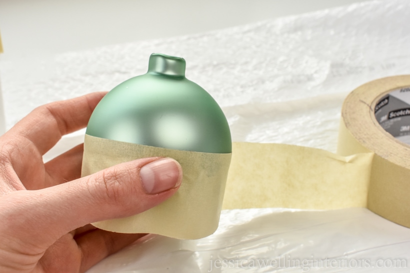 hand holding aqua ball ornament and wrapping masking tape around the middle