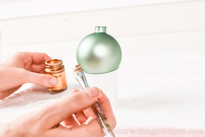 aqua-colored glass bauble sitting on a Dixie cup, ready to be painted with gold leaf paint