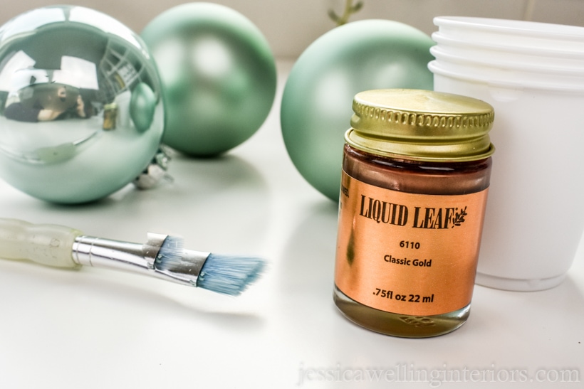 close-up of supplies to make easy diy kintsugi christmas ornaments: glass baubles, paintbrush, gold leaf paint, and dixie cups