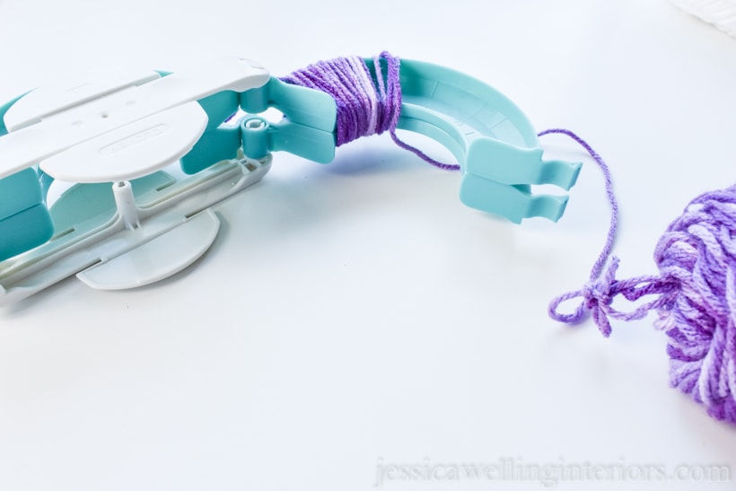 pom pom maker on a white background, with one arm extended and purple yarn wrapped around it