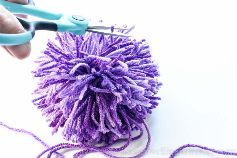 large purple pom pom being trimmed with a pair of craft scissors