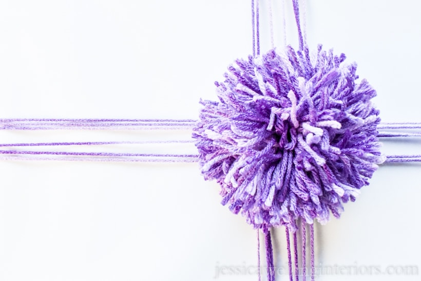 close-up of white wrapped gift tied with purple yarn and a giant purple pom pom