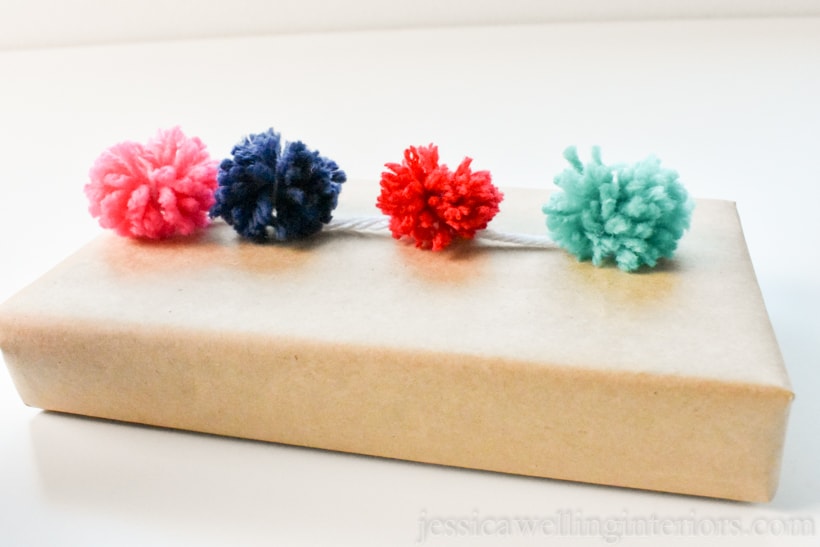 small gift box wrapped with recycled brown paper, with small pom pom garland attached to the top