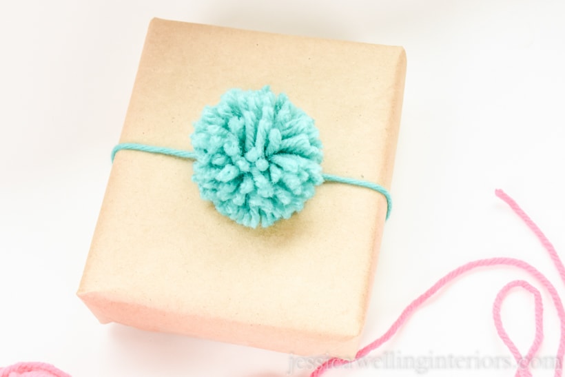 small brown paper parcel tied with aqua-colored yarn and a matching pompom