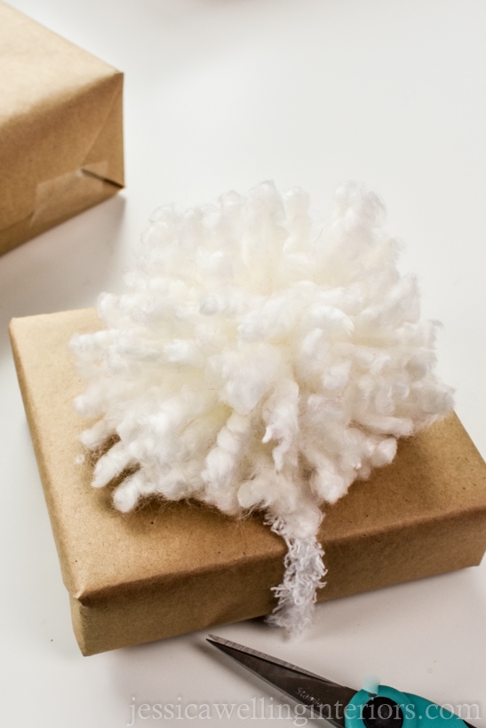 small brown wrapped gift with a large white fluffy pom pom on top