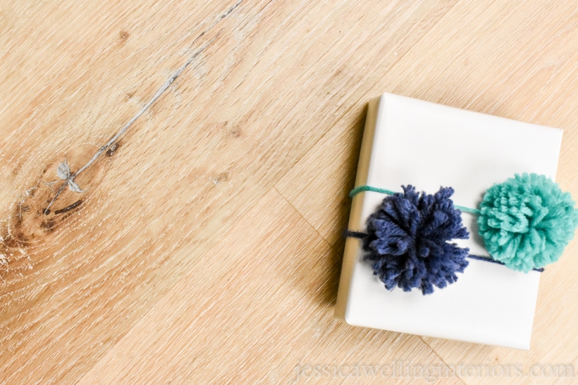 small white paper-wrapped gift with two pom poms on top- one navy blue and one aqua