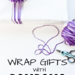 Wrap Gifts with Pom Poms: white background with white paper-wrapped gift, tied with purple yarn and large purple pom pom