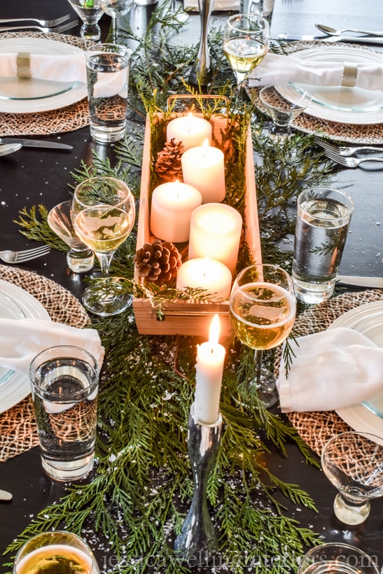 Christmas table decorations with simple cedar branches and a wood tray of candles and pinecones as a centerpiece