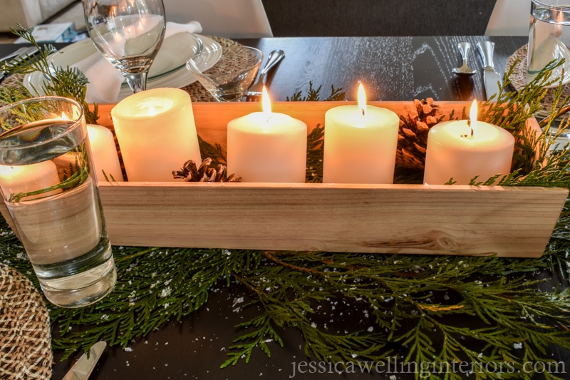 Christmas table decorations with wood tray full of white pillar candles and pine cones