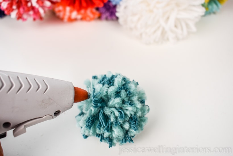 close-up of hot glue gun applying glue to a pom pom