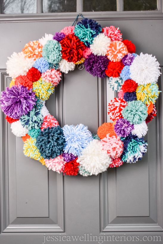 bright and colorful pom pom wreath hanging on a door for Christmas