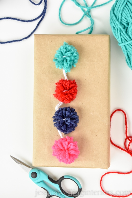 close-up of small parcel wrapped with brown paper and topped with a string of colorful mini pom poms