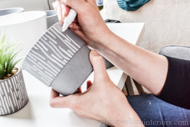 close-up of hands drawing vertical line pattern on a grey NYPON pot from IKEA with a white paint pen