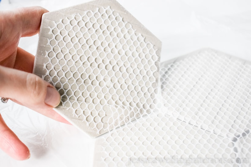 close-up of hands removing white hexagon tiles from mesh backing for making tile coasters