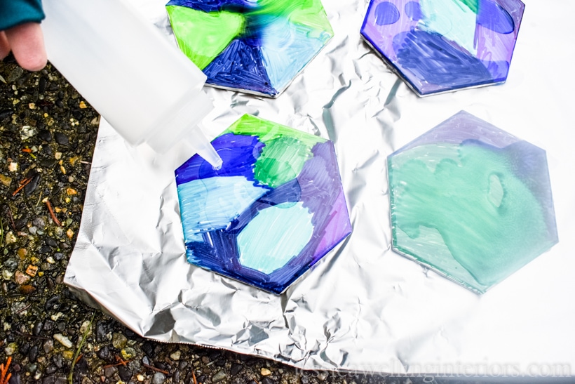 close-up of hand using squeeze bottle to drizzle alcohol onto tile coasters