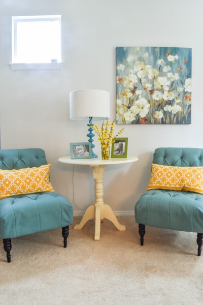 living room with two teal chairs, bright yellow throw pillows, and a colorful painting