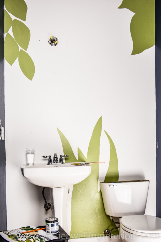 powder room wall painted white, with green leaves and grass to begin a hand-painted botanical mural