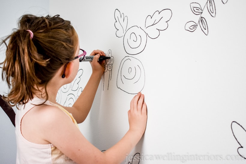 little girl drawing on walls with a black marker to create floral DIY wallpaper