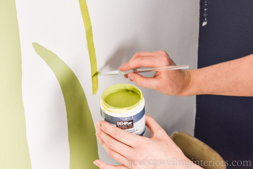 hand painting green stems on a  white wall to show how to paint a mural