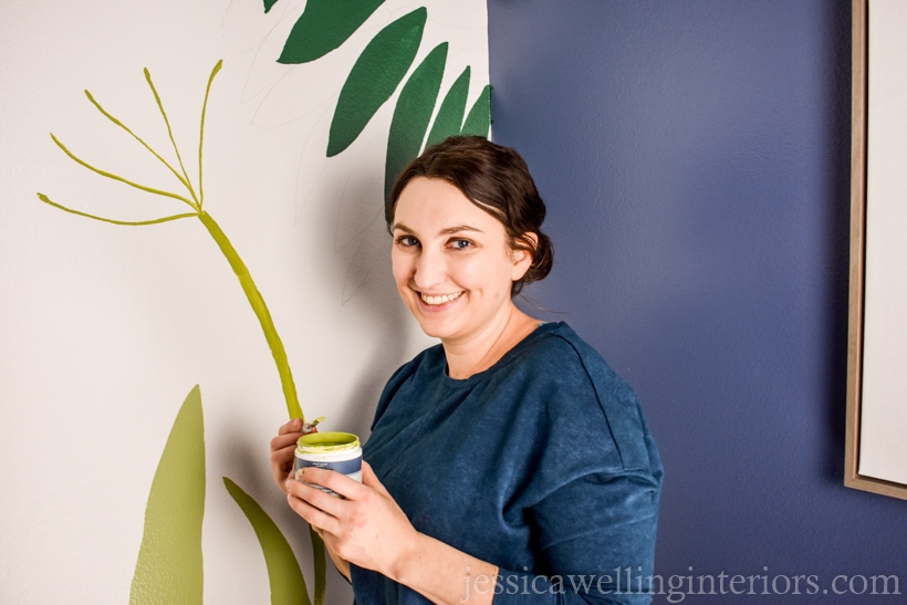 woman painting a mural accent wall in a small powder room with leaves and flowers