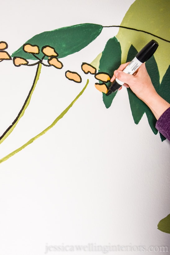 close-up of hand outlining yellow flowers with a black paint pen on a hand-painted mural in a small powder room