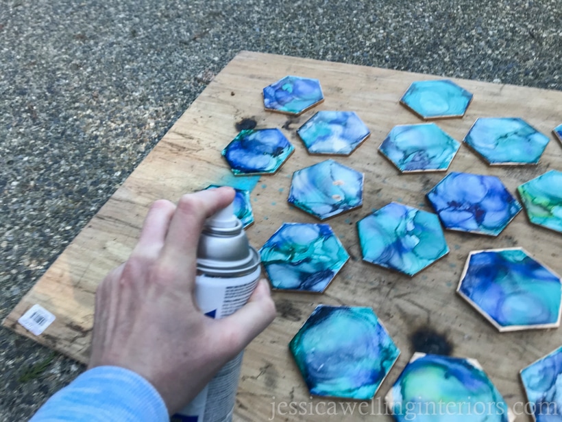 hand spray-painting clear coat on DIY tile coasters to make them waterproof