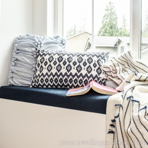 navy blue upholstered window seat cushion with throw pillows, a blanket, and a children's book