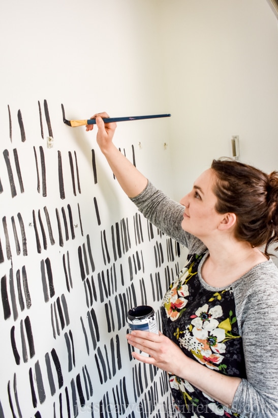 woman creating a painted accent wall with a modern black and white pattern