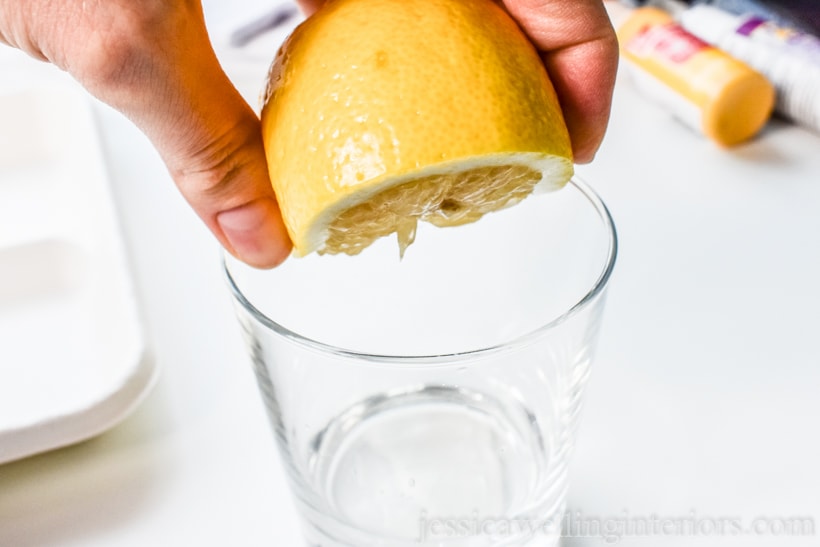 close-up of hand squeezing half a lemon into a small glass to prepare it for printing tea towels