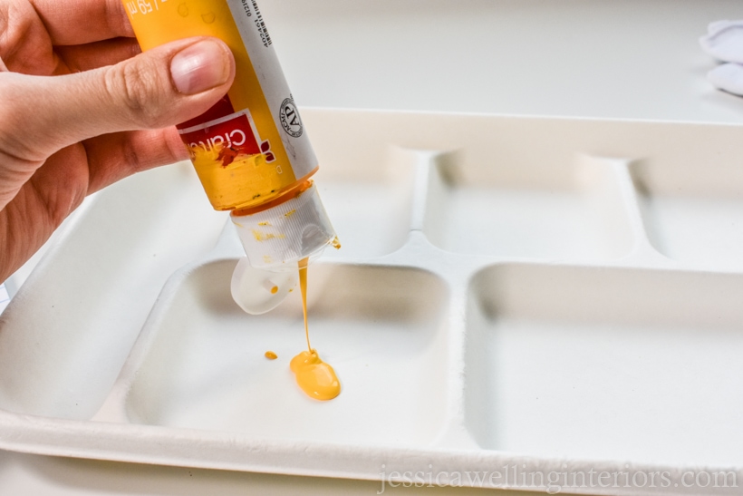 close-up of hand squeezing bottle of yellow acrylic paint onto a paper plate to paint lemon