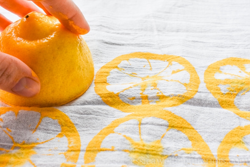 hand using a lemon half to print a pattern on a flour sack kitchen towel