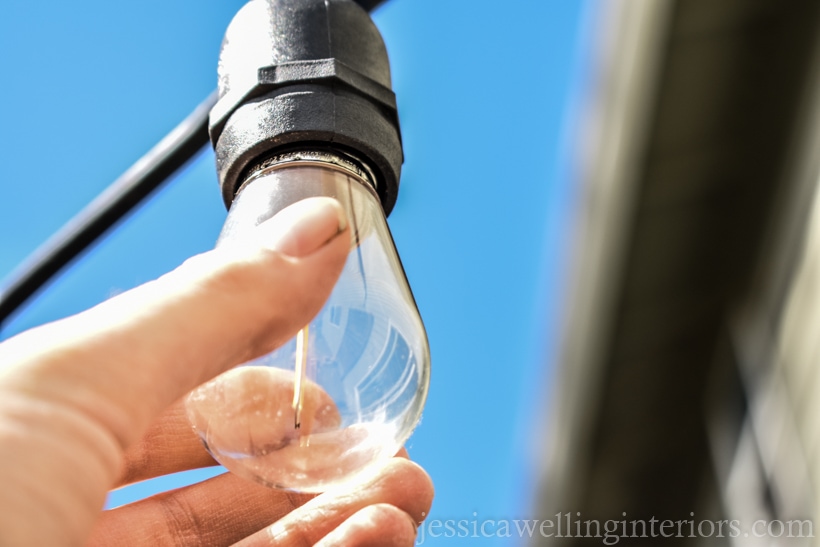 close-up of hand screwing light bulb into socket after outdoor string lights are hung over a deck