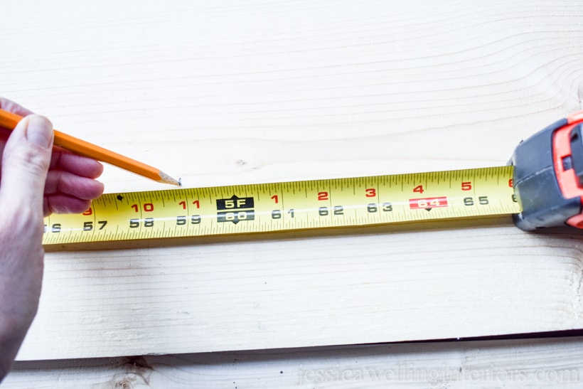 measuring tape and hand with pencil marking board to make DIY vertical garden planter