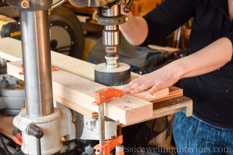 close-up of woman using drill press to cut hole in indoor vertical garden shelf to hold pots with faux hanging plants