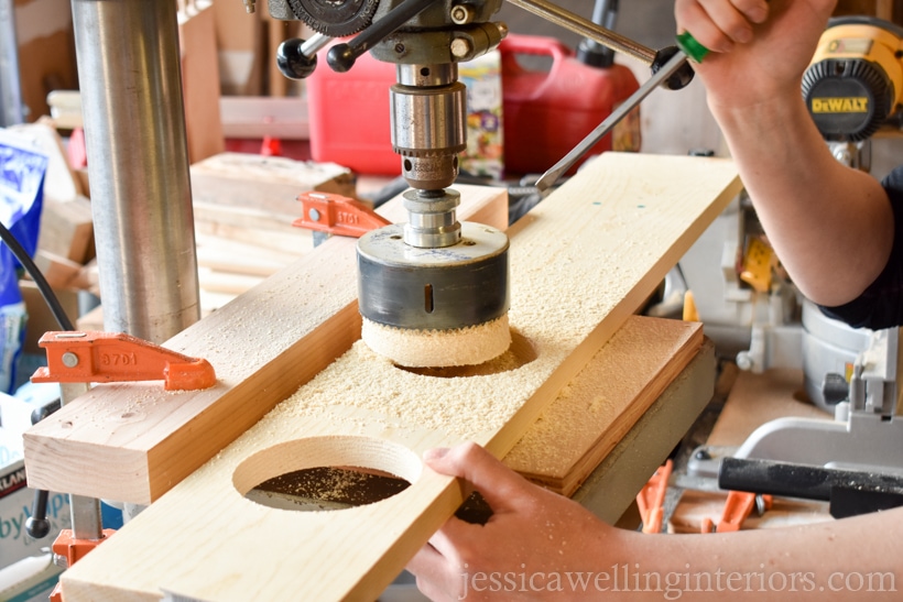 hands using screw driver to remove wood cutout from hole saw on a drill press to make a vertical garden