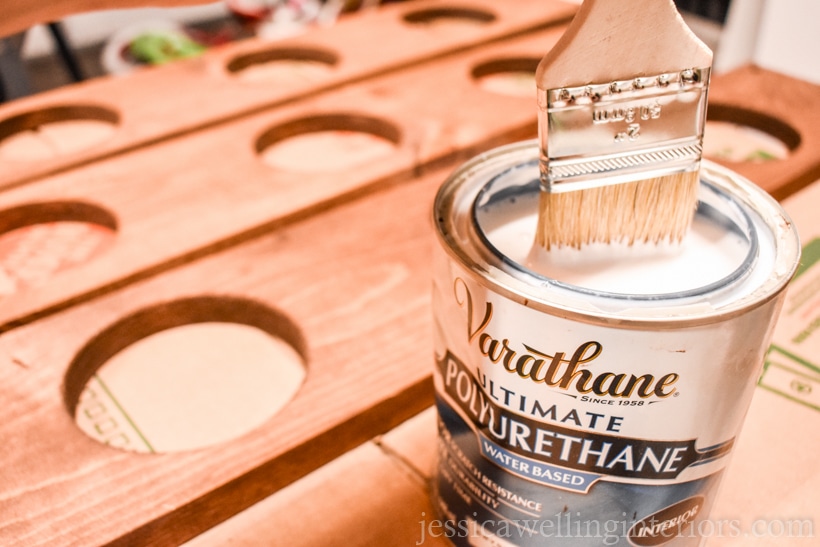 close-up of paintbrush being dipped into open can of Varathane polyurethane clear coat sealer with vertical garden shelves in the background