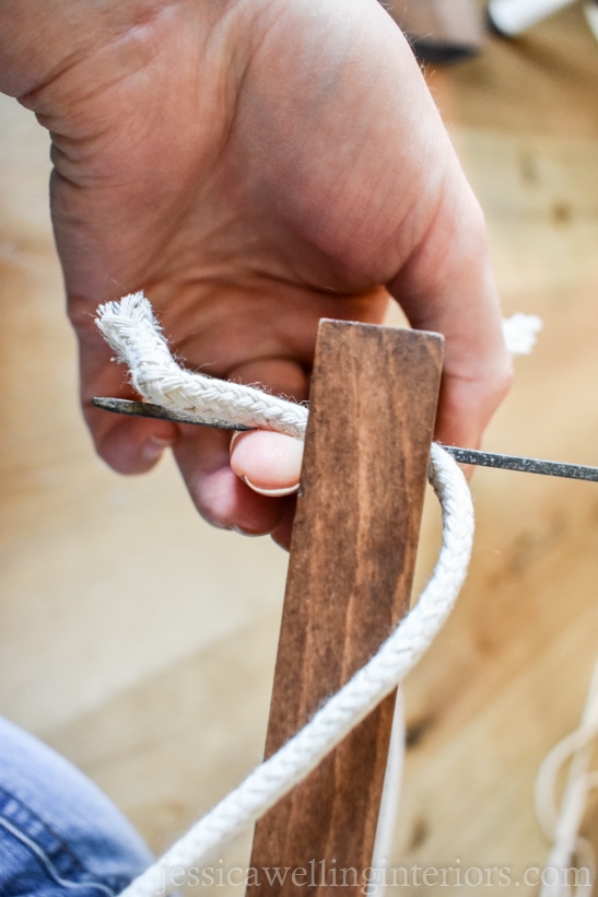 close-up of hand using a skewer to poke rope through a hole drilled in a vertical garden shelf