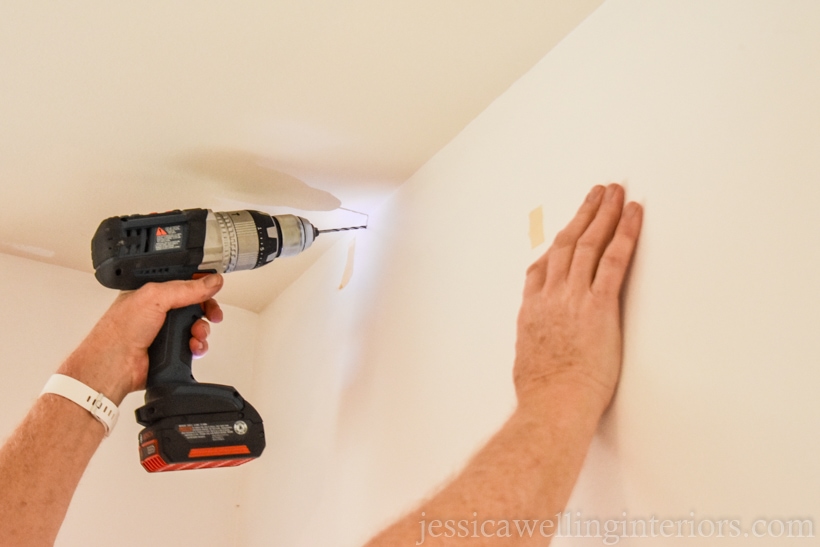 hand holding a drill, drilling into upper corner of a white wall to hang an artificial vertical garden