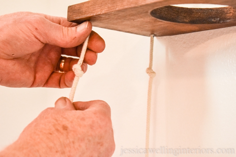 close-up of hands adjusting knots in the ropes suspending wood vertical garden shelves