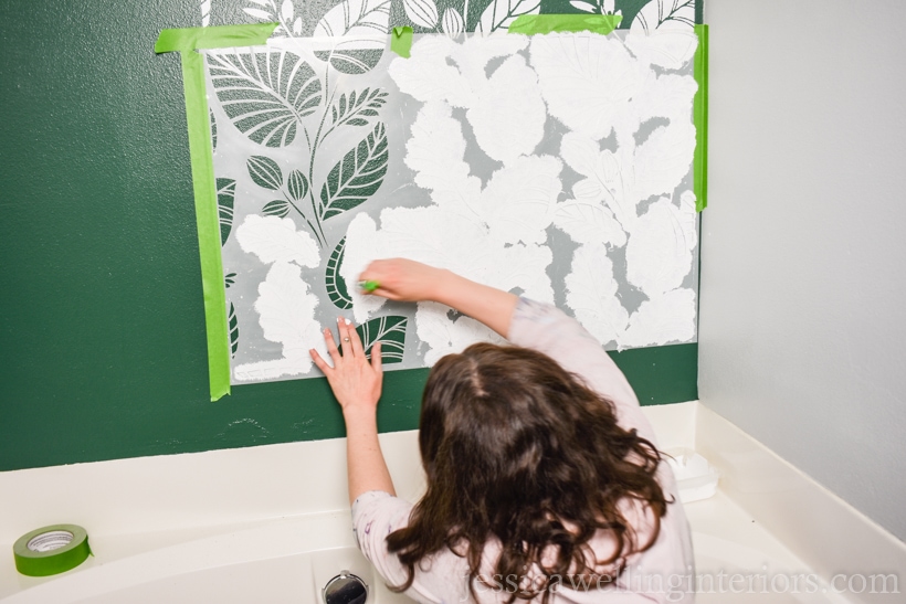 woman applying white paint to a wall stencil